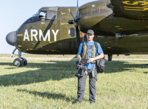 Michael Jensen with a camera rig in front of a vintage U.S. Army aircraft
