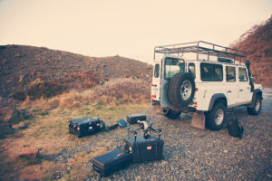 Camera cases and gear laid out beside a Land Rover Defender on location