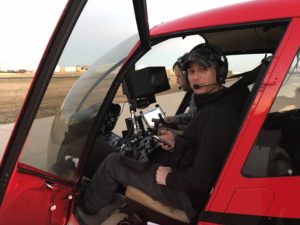 Camera operator with a gimbal controller seated in a red helicopter