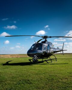 Dark helicopter with a camera gimbal parked on grass under a blue sky