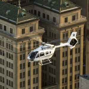 White Airbus H145 N945DC flying past tan buildings with green roofs