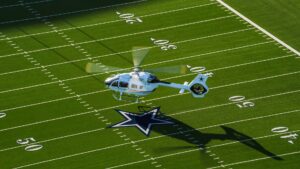 White helicopter flying over a football field with a star at midfield