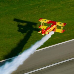 Red and yellow biplane trailing smoke over a runway