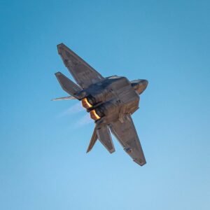 Fighter jet banking with afterburners against a blue sky