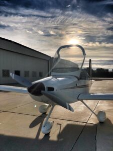 White single-engine airplane with canopy open on the tarmac at sunset