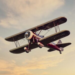 Maroon biplane climbing through a sunset sky