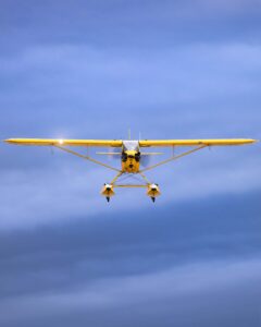 Yellow floatplane flying toward the camera against a blue sky