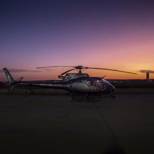 Two helicopters on the tarmac at sunset, one with a camera gimbal on the nose