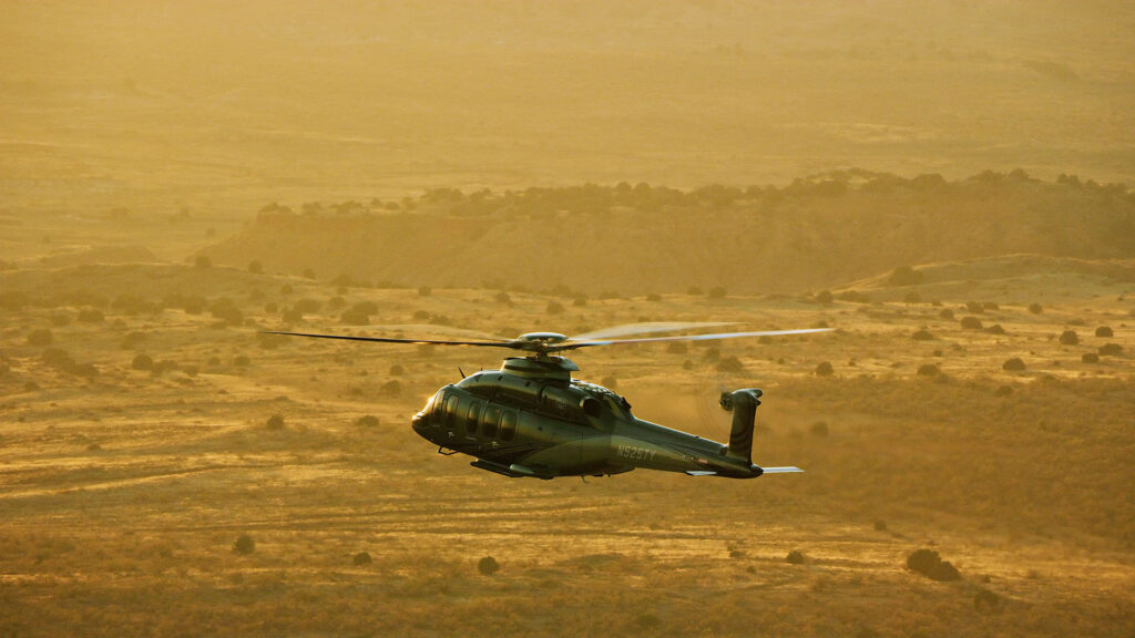 Bell 525 helicopter flying low over desert terrain at sunset