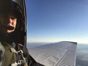 Helmeted camera operator leaning out of an aircraft in flight