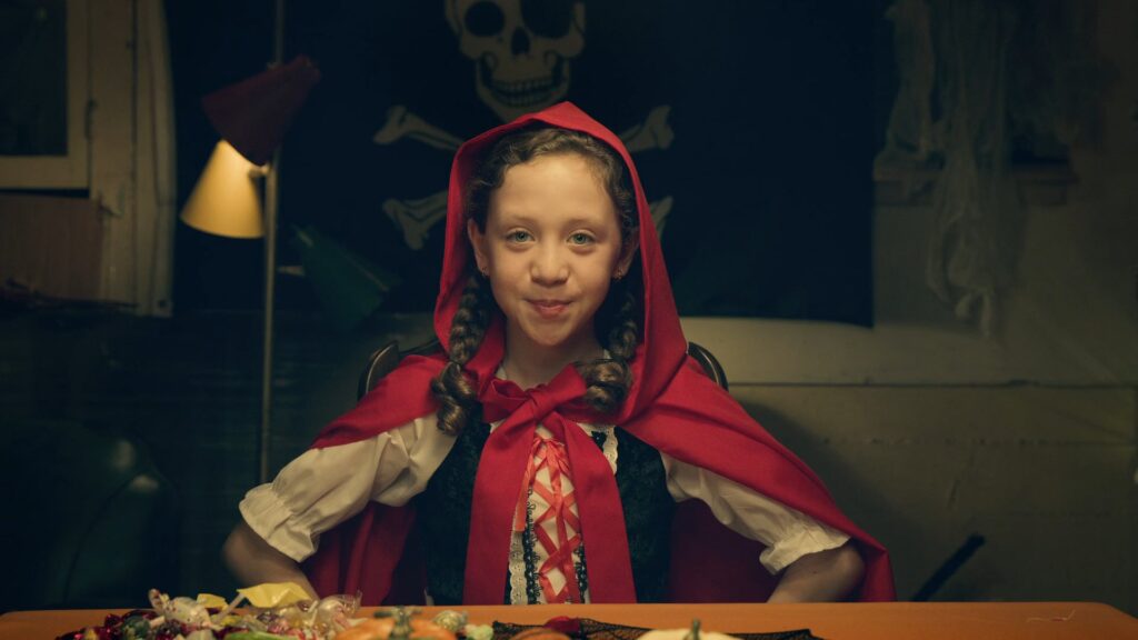 Girl in a red hooded cloak standing in a lamp-lit room