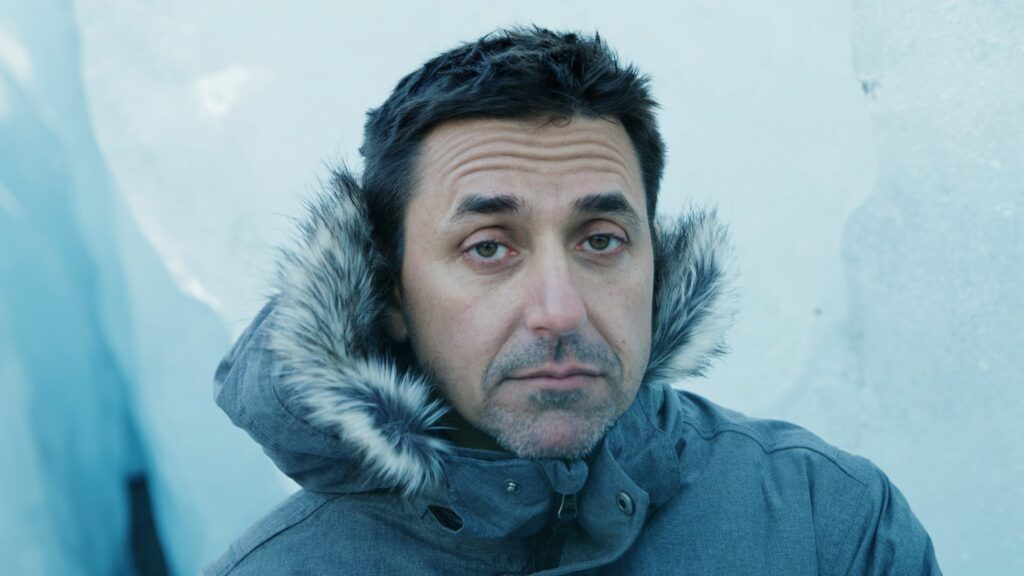 Man in a fur-lined parka hood in a cold blue-lit scene
