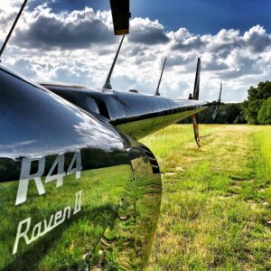 Camera pod mounted on a Robinson R44 flying over a grass field