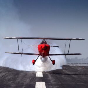Red aerobatic biplane blowing smoke on a runway