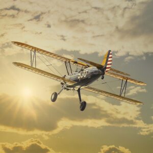Blue and yellow Stearman biplane flying toward sunset