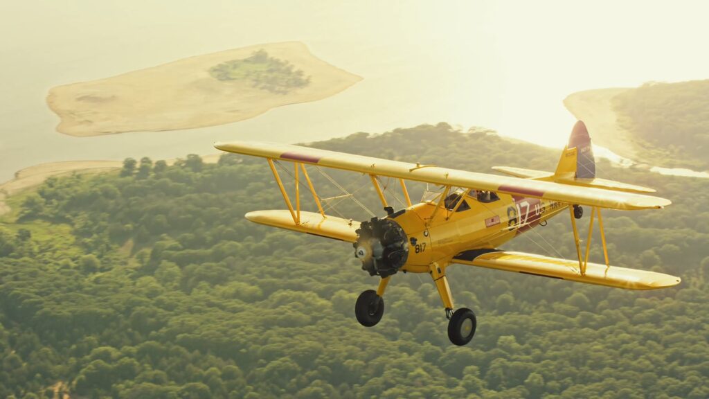 Yellow Stearman biplane flying along a coastline