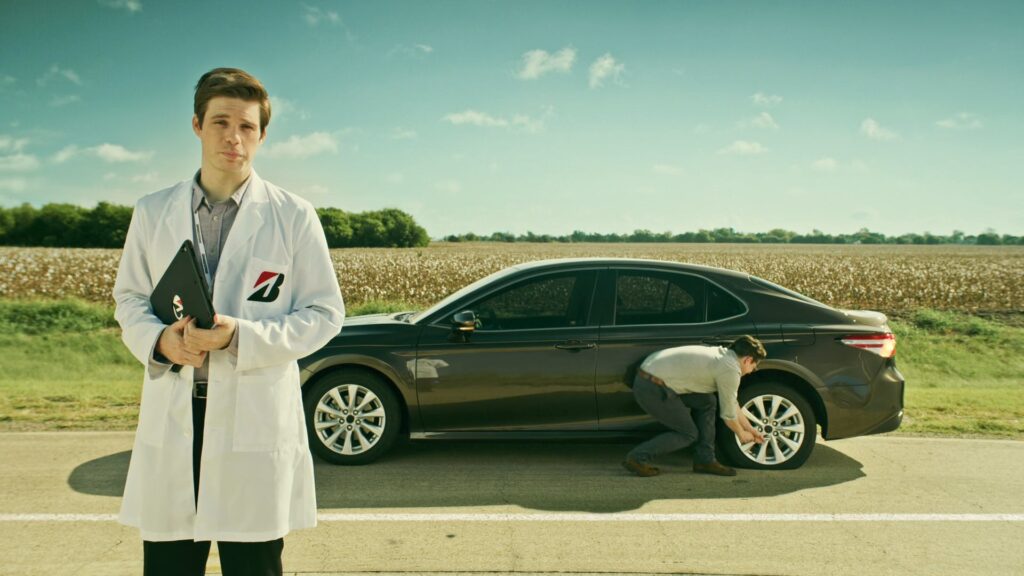 Technician in a lab coat presenting a car in an open field