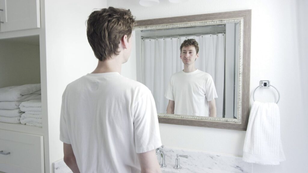Young man looking at his reflection in a bathroom mirror