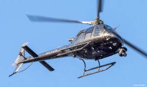 Dark helicopter with a camera gimbal in flight against a blue sky