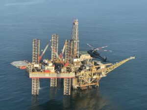 Dark helicopter hovering beside an offshore oil rig