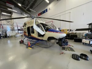Cream helicopter with a nose gimbal being prepped inside a hangar