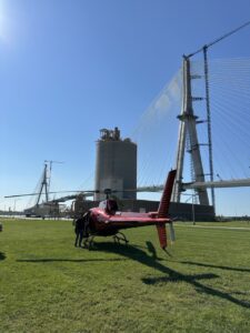 Red helicopter on grass in front of a cable-stayed bridge