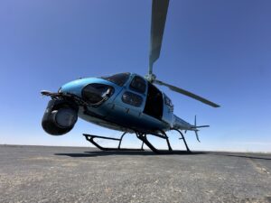 Light blue helicopter with a camera gimbal parked on the tarmac