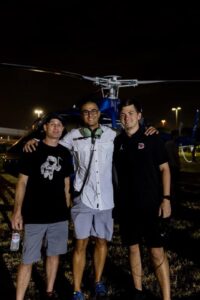Three men posing at night in front of a blue helicopter