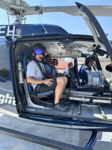 Crew inside a navy helicopter, one wearing a helmet with a purple visor